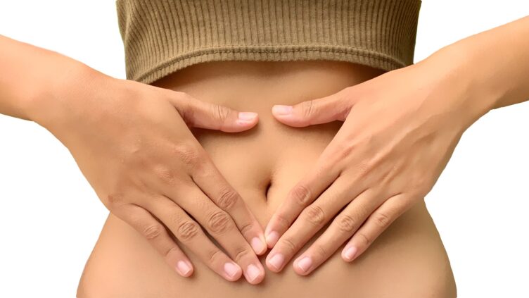 Person massaging their lower abdomen with both hands, bare midriff visible under a brown top.