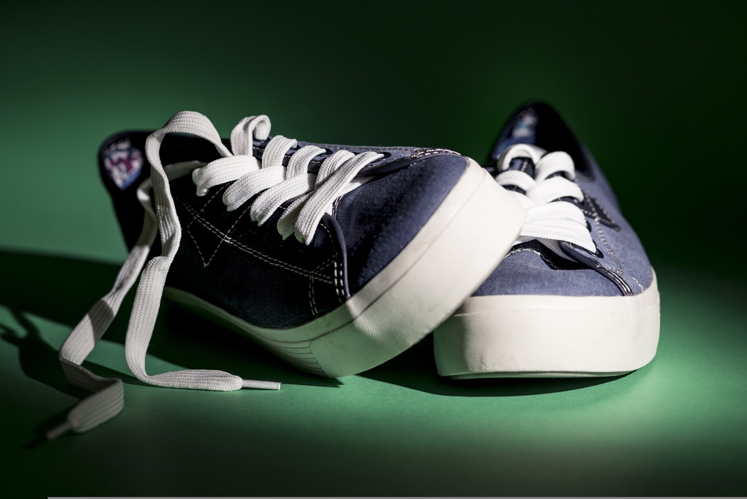 Close-up of navy blue sneakers with white laces resting on a green surface.